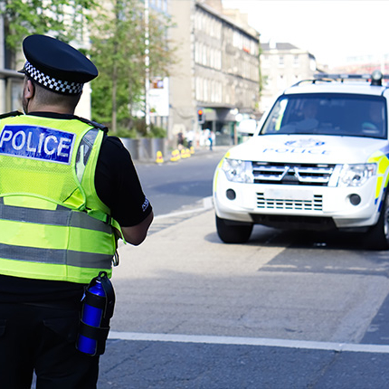 brittish police officer standing in front of his police car on a city road